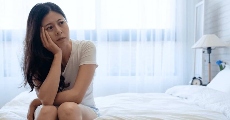 Femme assise sur son lit avec un air maussade