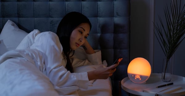 Woman on her phone in bed with a low lighting